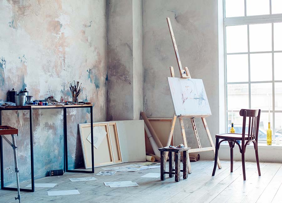 Bright room with large window displaying an artist's canvas and art supplies strewn about the table and floor.
