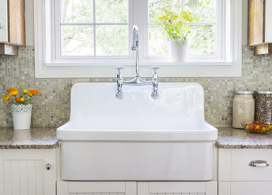 Farmhouse sink flanked by granite counter tops with a mosaic tile backsplash beneath a bright open window